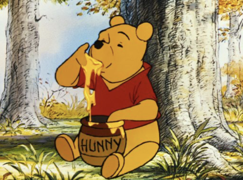 Winnie l'Ourson est assise sur l'herbe dans une forêt, plongeant sa patte dans un pot étiqueté "Hunny" et mangeant le miel, comme il l'a fait lors de sa première sortie le 4 février 1966.