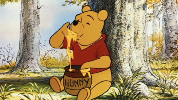 Winnie l'Ourson est assise sur l'herbe dans une forêt, plongeant sa patte dans un pot étiqueté "Hunny" et mangeant le miel, comme il l'a fait lors de sa première sortie le 4 février 1966.