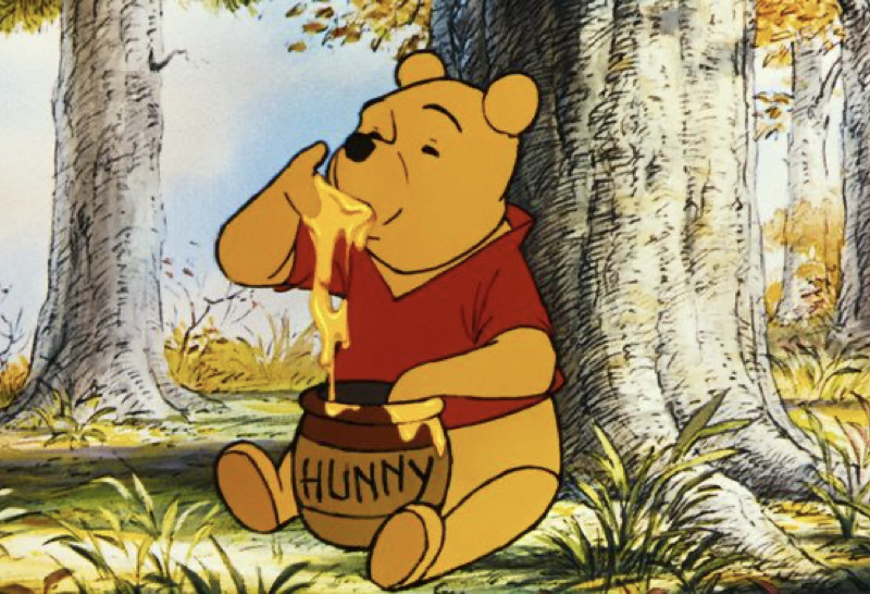 Winnie l'Ourson est assise sur l'herbe dans une forêt, plongeant sa patte dans un pot étiqueté "Hunny" et mangeant le miel, comme il l'a fait lors de sa première sortie le 4 février 1966.