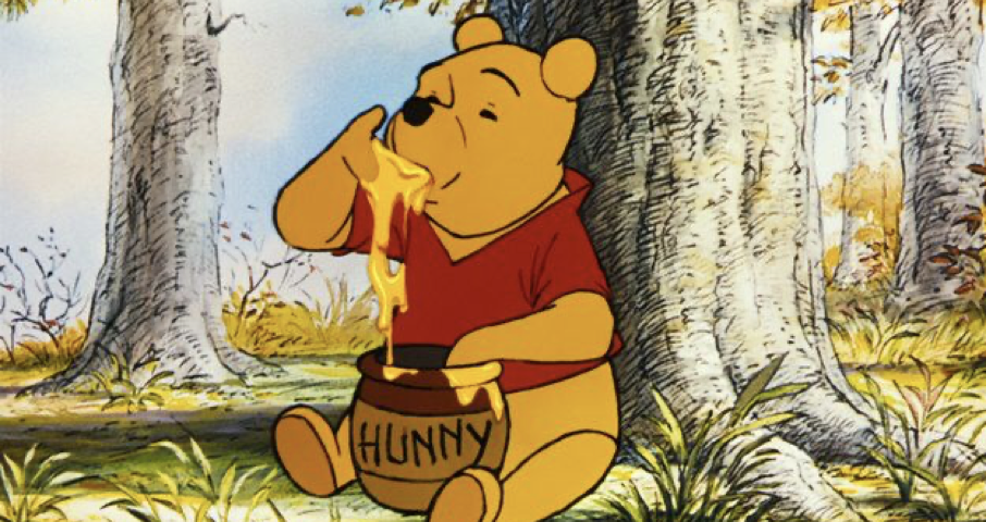 Winnie l'Ourson est assise sur l'herbe dans une forêt, plongeant sa patte dans un pot étiqueté "Hunny" et mangeant le miel, comme il l'a fait lors de sa première sortie le 4 février 1966.