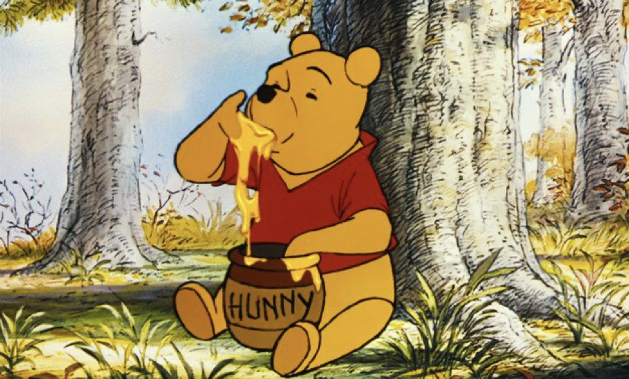 Winnie l'Ourson est assise sur l'herbe dans une forêt, plongeant sa patte dans un pot étiqueté "Hunny" et mangeant le miel, comme il l'a fait lors de sa première sortie le 4 février 1966.