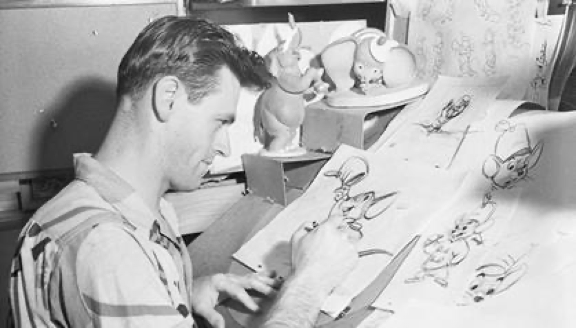 Un animateur dessine des croquis de personnages de dessins animés à un bureau entouré de modèles de référence et de dessins, dont des illustrations inspirées de Winnie l'Ourson et célébrant la sortie de son film le 4 février 1966.