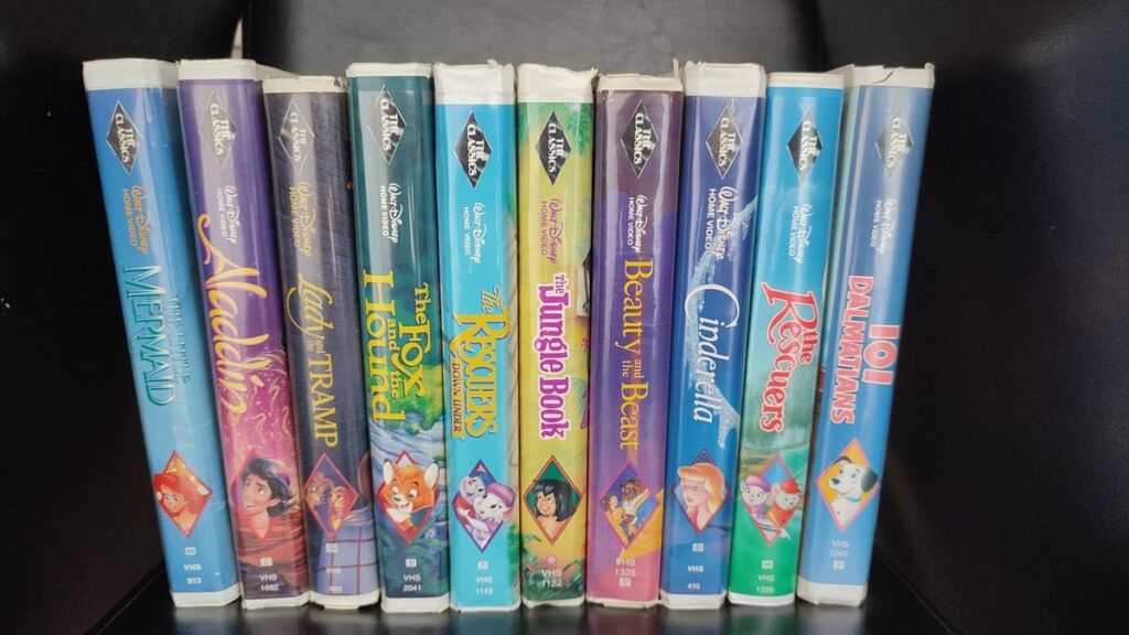 Une collection de onze cassettes Disney Black Diamond VHS, dont La Belle et la Bête, La Petite Sirène, Aladdin et bien d'autres encore, toutes des VHS rares et précieuses, disposées côte à côte sur une étagère noire.