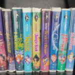 Une collection de onze cassettes Disney Black Diamond VHS, dont La Belle et la Bête, La Petite Sirène, Aladdin et bien d'autres encore, toutes des VHS rares et précieuses, disposées côte à côte sur une étagère noire.