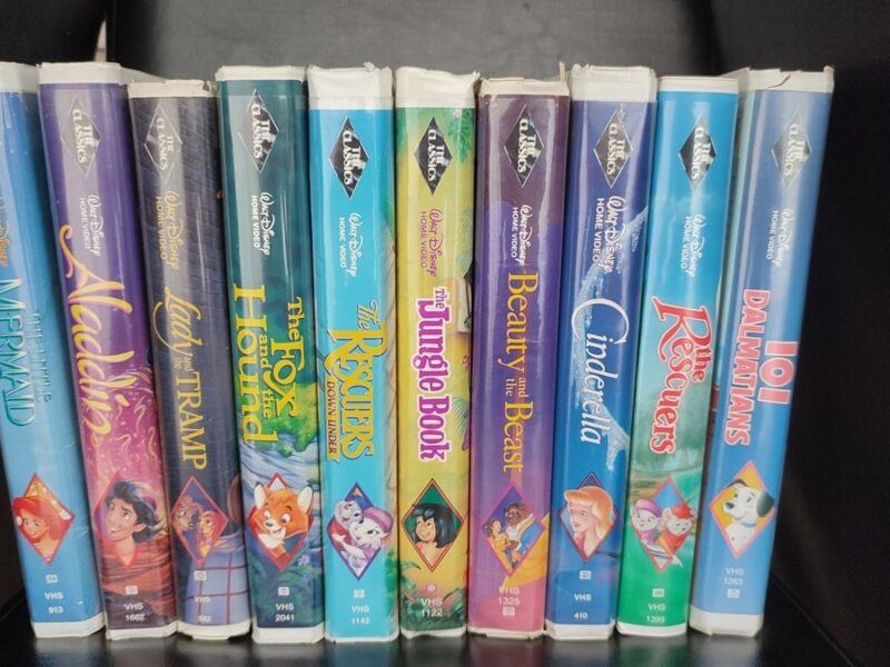 Une collection de onze cassettes Disney Black Diamond VHS, dont La Belle et la Bête, La Petite Sirène, Aladdin et bien d'autres encore, toutes des VHS rares et précieuses, disposées côte à côte sur une étagère noire.