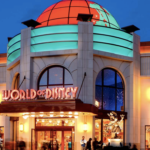 Vue extérieure d'une boutique World of Disney éclairée de nuit, avec un dôme illuminé, des fenêtres cintrées et des enseignes colorées. Idéal pour acheter des souvenirs de Disneyland Paris après une journée magique au parc Disneyland Paris.