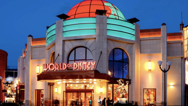 Vue extérieure d'une boutique World of Disney éclairée de nuit, avec un dôme illuminé, des fenêtres cintrées et des enseignes colorées. Idéal pour acheter des souvenirs de Disneyland Paris après une journée magique au parc Disneyland Paris.