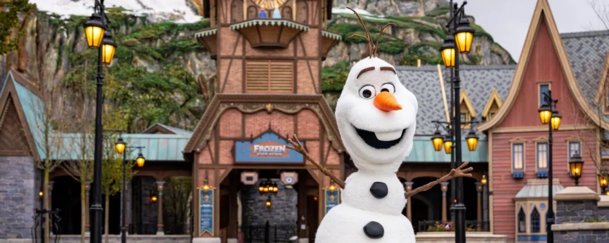 Une personne déguisée en bonhomme de neige Olaf se tient les bras ouverts devant un bâtiment sur le thème de Frozen à Disneyland Paris, qui accueillera bientôt le Monde de la Reine des Neiges lors de son ouverture le 29 mars 2026.