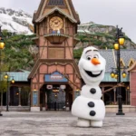 Une personne déguisée en bonhomme de neige Olaf se tient les bras ouverts devant un bâtiment sur le thème de Frozen à Disneyland Paris, qui accueillera bientôt le Monde de la Reine des Neiges lors de son ouverture le 29 mars 2026.