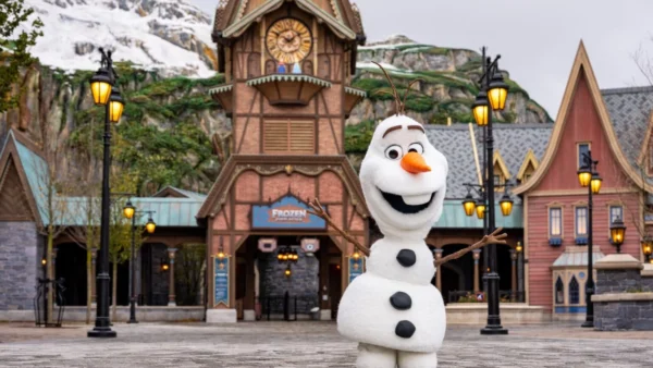 Une personne déguisée en bonhomme de neige Olaf se tient les bras ouverts devant un bâtiment sur le thème de Frozen à Disneyland Paris, qui accueillera bientôt le Monde de la Reine des Neiges lors de son ouverture le 29 mars 2026.
