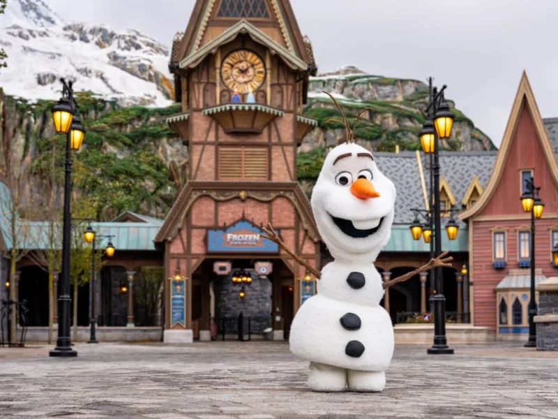 Une personne déguisée en bonhomme de neige Olaf se tient les bras ouverts devant un bâtiment sur le thème de Frozen à Disneyland Paris, qui accueillera bientôt le Monde de la Reine des Neiges lors de son ouverture le 29 mars 2026.