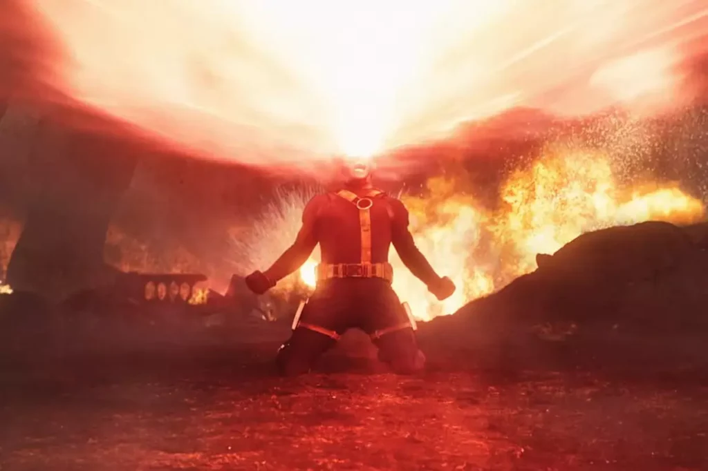 Une personne vêtue d'un costume rouge est agenouillée sur le sol, émettant un large faisceau d'énergie à partir de ses yeux dans un environnement enflammé et enfumé - rappelant les teasers dramatiques d'Avengers Doomsday.