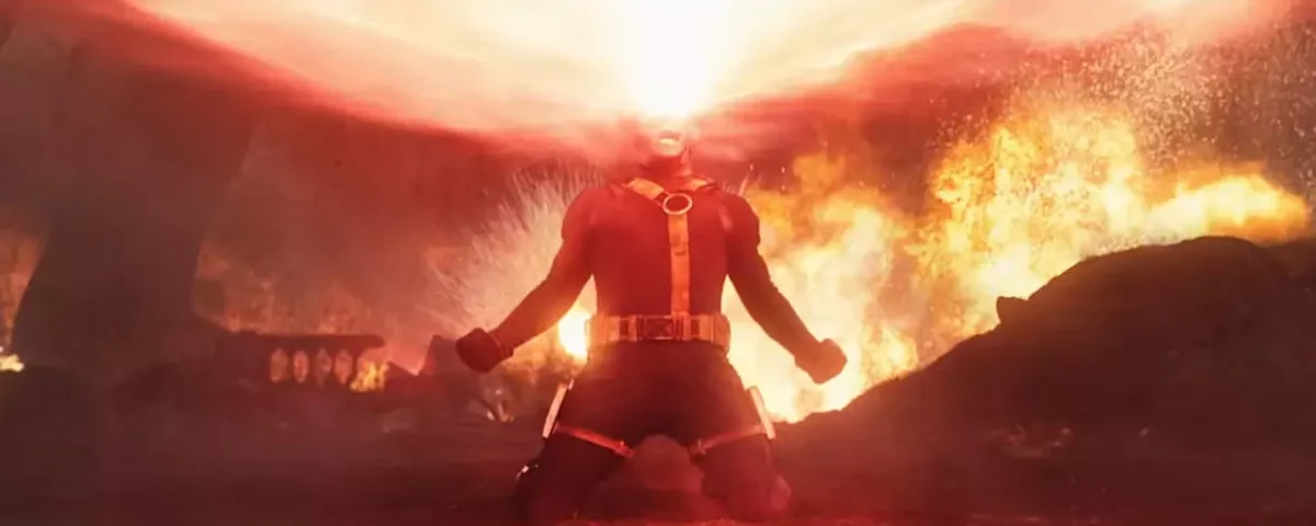 Une personne vêtue d'un costume rouge est agenouillée sur le sol, émettant un large faisceau d'énergie à partir de ses yeux dans un environnement enflammé et enfumé - rappelant les teasers dramatiques d'Avengers Doomsday.
