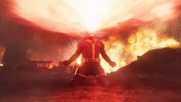 Une personne vêtue d'un costume rouge est agenouillée sur le sol, émettant un large faisceau d'énergie à partir de ses yeux dans un environnement enflammé et enfumé - rappelant les teasers dramatiques d'Avengers Doomsday.