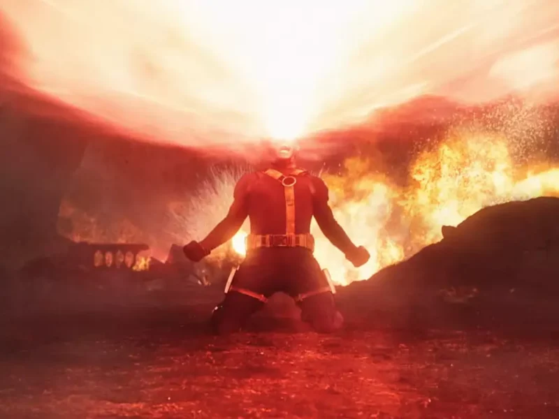 Une personne vêtue d'un costume rouge est agenouillée sur le sol, émettant un large faisceau d'énergie à partir de ses yeux dans un environnement enflammé et enfumé - rappelant les teasers dramatiques d'Avengers Doomsday.
