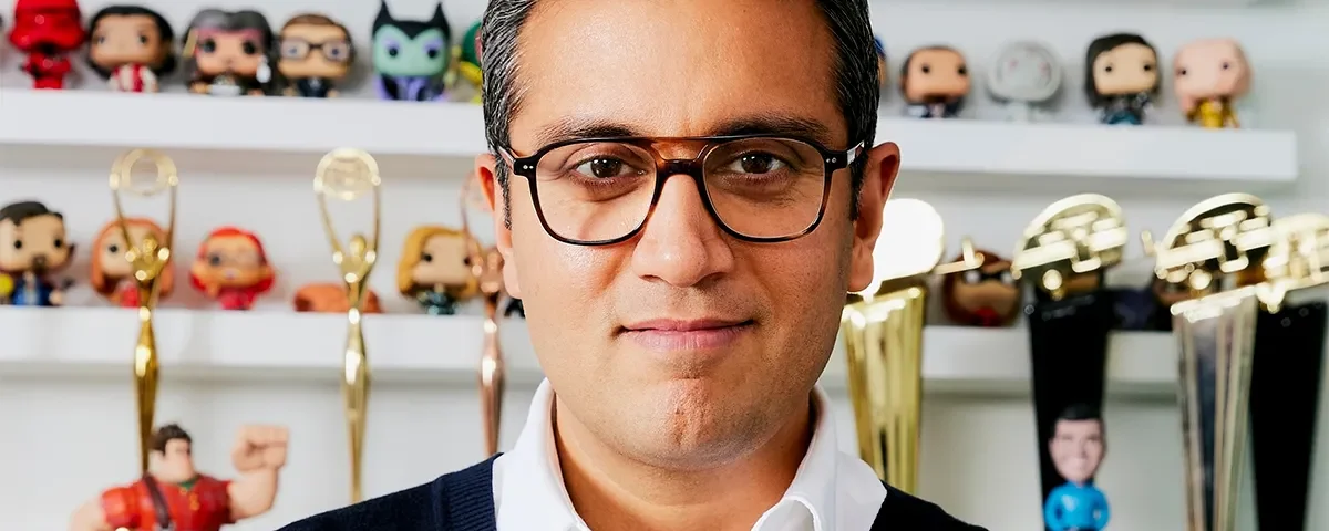Le directeur marketing de Disney, Asad Ayaz, portant des lunettes, se tient devant des étagères présentant des figurines de collection et plusieurs récompenses en or.