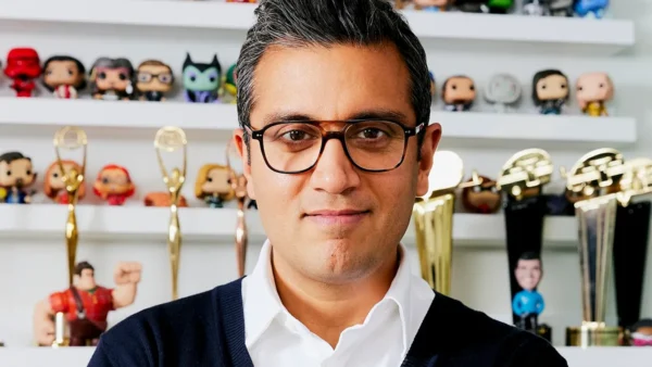 Le directeur marketing de Disney, Asad Ayaz, portant des lunettes, se tient devant des étagères présentant des figurines de collection et plusieurs récompenses en or.