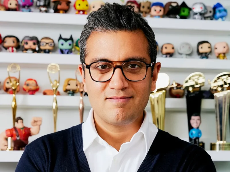 Le directeur marketing de Disney, Asad Ayaz, portant des lunettes, se tient devant des étagères présentant des figurines de collection et plusieurs récompenses en or.