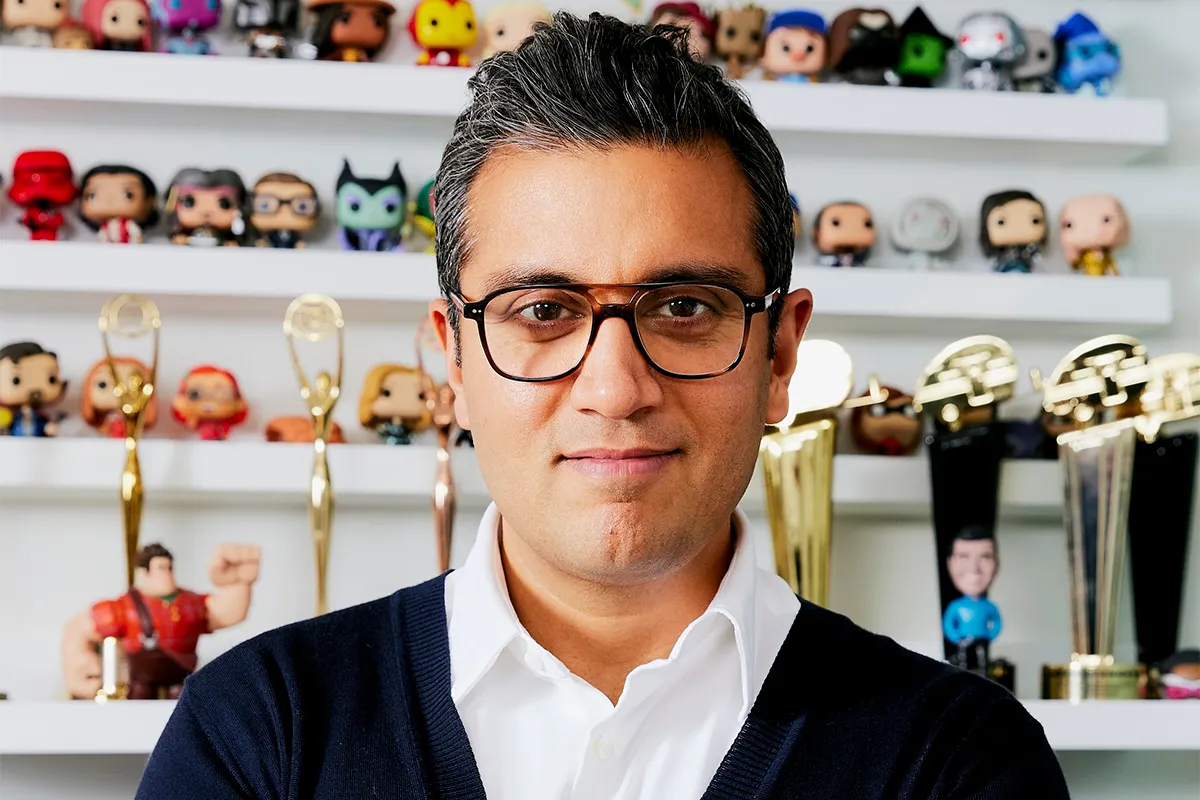 Le directeur marketing de Disney, Asad Ayaz, portant des lunettes, se tient devant des étagères présentant des figurines de collection et plusieurs récompenses en or.