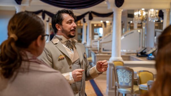 Un homme en costume beige s'adresse à deux personnes dans une salle décorée et élégante avec des colonnes, des chaises et des tissus drapés lors d'un événement de recrutement à Villeurbanne.