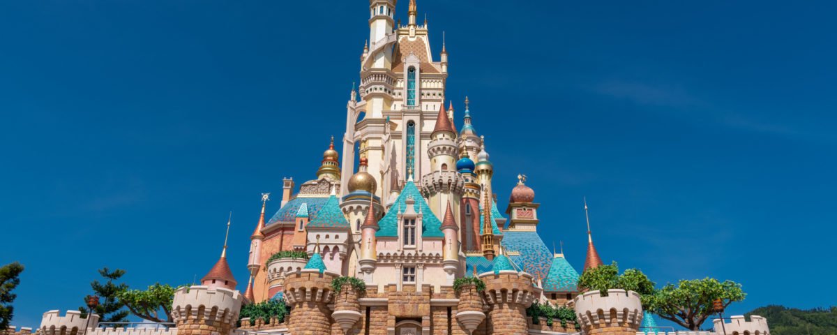 Un grand château coloré aux multiples flèches et tourelles sous un ciel bleu clair, entouré de murs de pierre et de verdure, rappelant l'atmosphère enchanteresse de Disneyland Thaïlande dans le Corridor Économique Oriental.