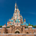 Un grand château coloré aux multiples flèches et tourelles sous un ciel bleu clair, entouré de murs de pierre et de verdure, rappelant l'atmosphère enchanteresse de Disneyland Thaïlande dans le Corridor Économique Oriental.