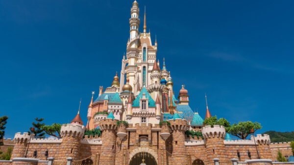 Un grand château coloré aux multiples flèches et tourelles sous un ciel bleu clair, entouré de murs de pierre et de verdure, rappelant l'atmosphère enchanteresse de Disneyland Thaïlande dans le Corridor Économique Oriental.