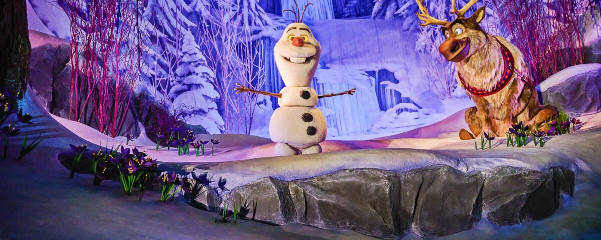 Olaf le bonhomme de neige et Sven le renne se trouvent sur une scène enneigée à Disney Adventure World, entourés de paysages hivernaux tels que des arbres couverts de neige et une cascade gelée en arrière-plan.