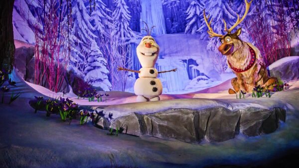 Olaf le bonhomme de neige et Sven le renne se trouvent sur une scène enneigée à Disney Adventure World, entourés de paysages hivernaux tels que des arbres couverts de neige et une cascade gelée en arrière-plan.