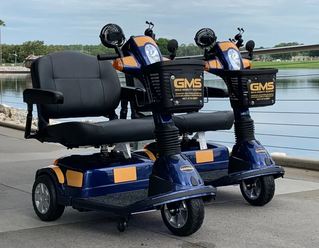 Deux scooters électriques de location bleus et orange portant l'inscription GMS sont garés côte à côte sur une allée pavée près d'un plan d'eau à Chalifert, non loin de Disneyland Paris.