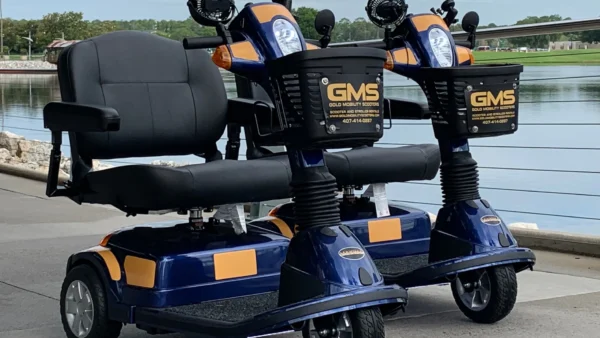 Deux scooters électriques de location bleus et orange portant l'inscription GMS sont garés côte à côte sur une allée pavée près d'un plan d'eau à Chalifert, non loin de Disneyland Paris.