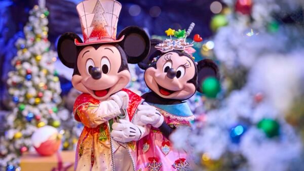 Mickey Mouse et Minnie Mouse en costumes de fête se tiennent ensemble devant des arbres de Noël décorés et des lumières de Noël lors des spectacles saisonniers à Disneyland Paris.