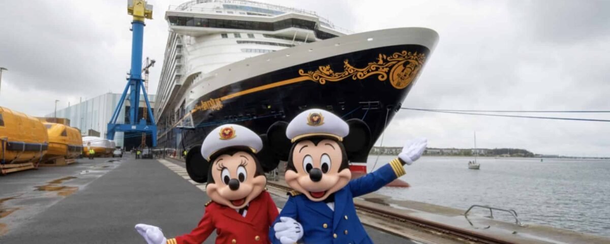 Deux personnes déguisées en Mickey et Minnie Mouse en uniforme de capitaine posent devant un grand bateau de croisière Disney Adventure amarré dans un port par une journée nuageuse.