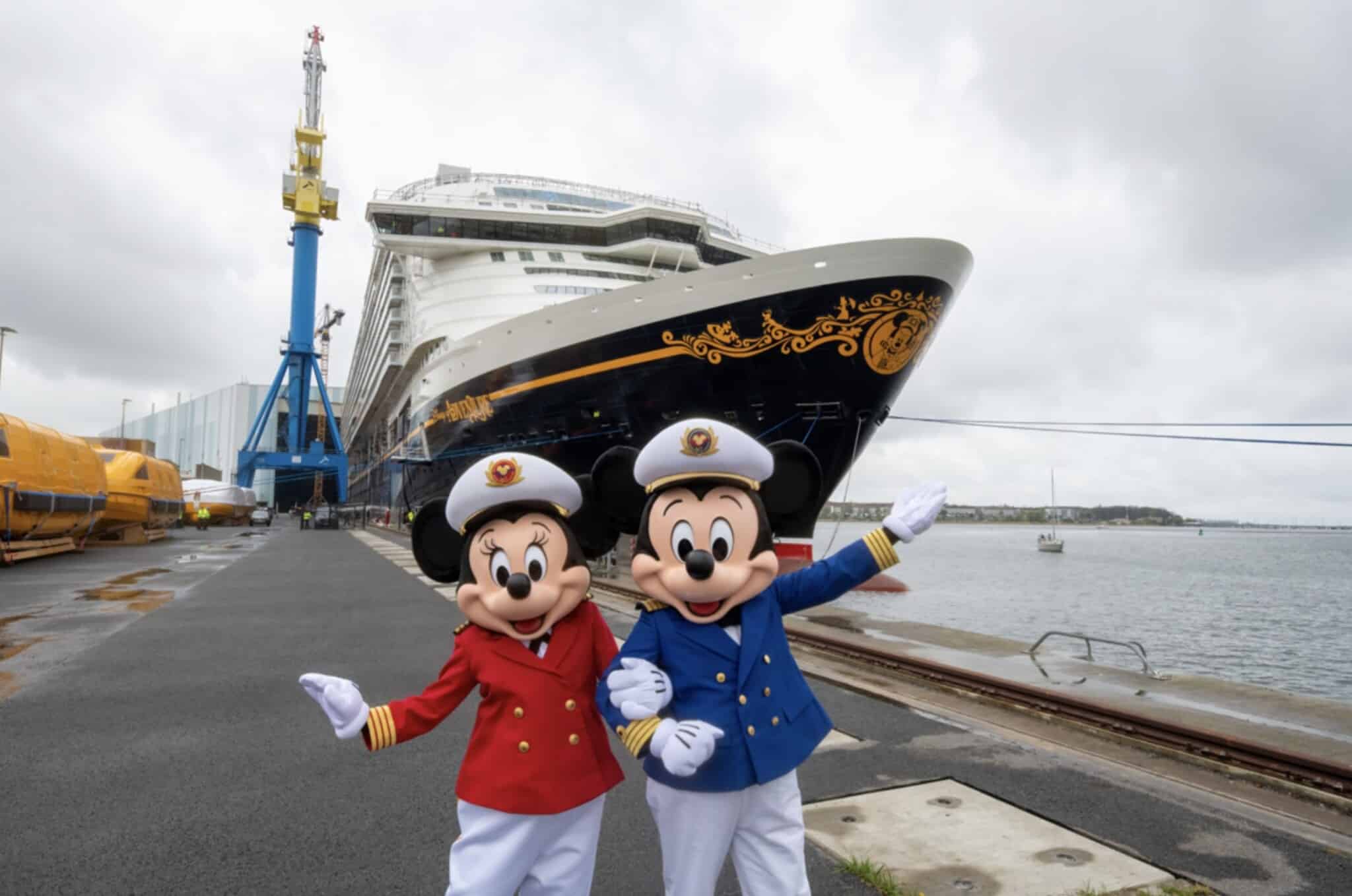Deux personnes déguisées en Mickey et Minnie Mouse en uniforme de capitaine posent devant un grand bateau de croisière Disney Adventure amarré dans un port par une journée nuageuse.