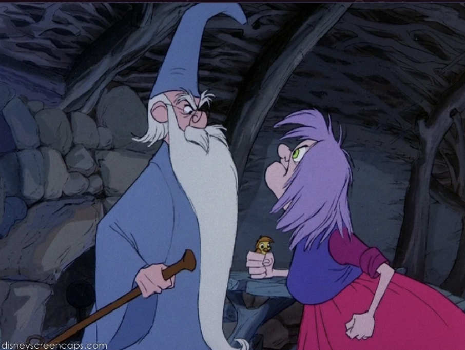 Un vieil homme vêtu d'une robe et d'un chapeau bleus, ressemblant à Merlin L'Enchanteur, fait face à une femme aux cheveux violets et à la robe rouge, tous deux semblant se disputer à l'intérieur d'une pièce rustique aux murs de pierre.