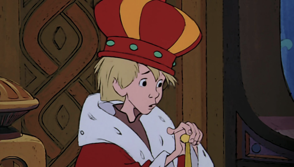 Un jeune personnage animé, portant une couronne et une robe royale et tenant un bâton, se tient à l'intérieur à côté d'un mur en bois avec des motifs sculptés - évoquant le monde magique de Merlin L'Enchanteur, sorti le 25 Décembre 1963.
