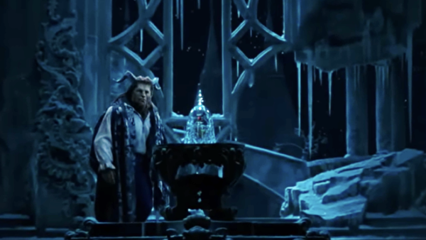 Un interprète costumé se tient à côté d'une rose en verre sur la scène, entouré de décors glacés de style gothique sous un éclairage bleu, évoquant la nostalgie des actions classiques en direct de Disney avec un approfondissement émotionnel.