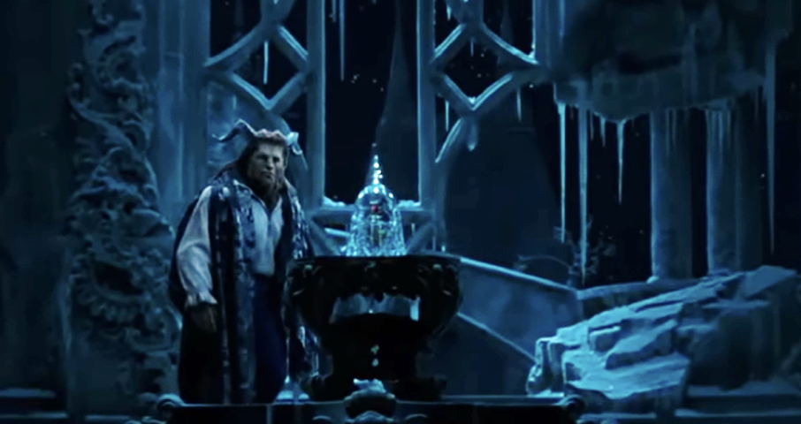 Un interprète costumé se tient à côté d'une rose en verre sur la scène, entouré de décors glacés de style gothique sous un éclairage bleu, évoquant la nostalgie des actions classiques en direct de Disney avec un approfondissement émotionnel.