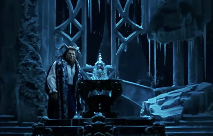 Un interprète costumé se tient à côté d'une rose en verre sur la scène, entouré de décors glacés de style gothique sous un éclairage bleu, évoquant la nostalgie des actions classiques en direct de Disney avec un approfondissement émotionnel.