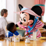 Une Minnie Mouse costumée accueille deux enfants à une table de restaurant pendant que les adultes regardent ; le petit déjeuner et les boissons sont sur la table - parfait pour les familles qui profitent du Free Dining Disney ou qui explorent les offres du Plan Repas Hôtels Disney.