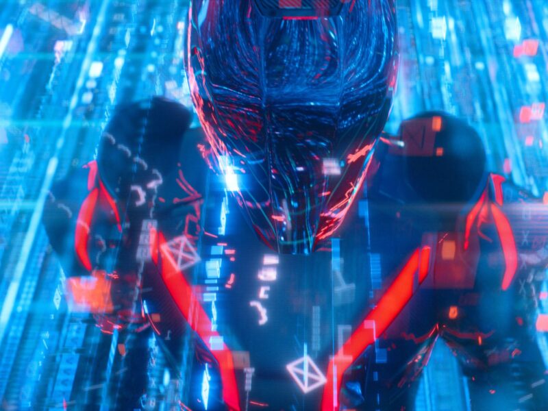 Une figure humanoïde futuriste aux accents rouge et bleu se tient dans un environnement numérique rempli de données flottantes et de néons, évoquant la saga Tron et le prochain Tron Ares sur Disney+.