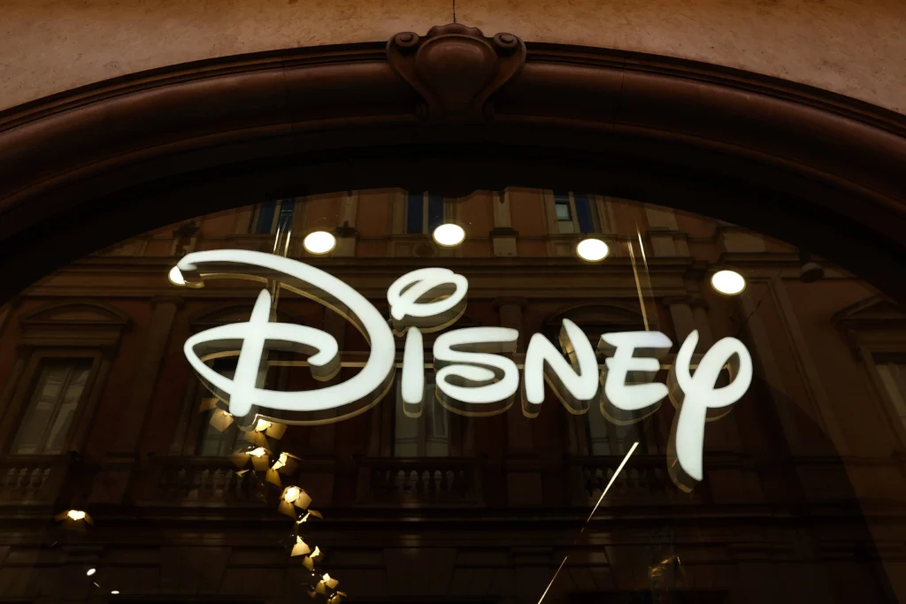 Un logo Disney blanc est éclairé sur une façade en verre, reflétant un bâtiment avec des fenêtres et des détails architecturaux, tout en faisant allusion à l'innovation observée dans Seedance 2.0 de Bytedance.