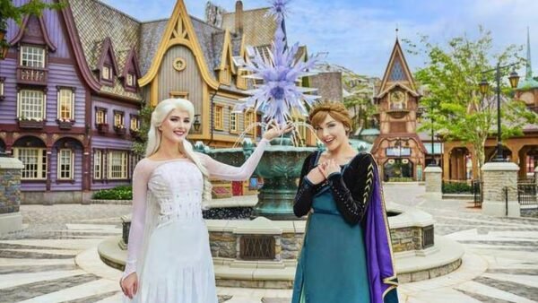 Deux femmes déguisées en Elsa et Anna de La Reine des Neiges posent devant une fontaine à thème et des bâtiments de style villageois, capturant la magie des attractions de Disneyland Paris.
