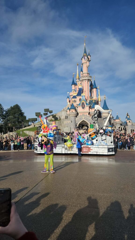Un char de parade animé par les personnages de Disney Pixar passe devant le château de la Belle au bois dormant à Disneyland Paris, tandis qu'un artiste costumé divertit la foule captivée.