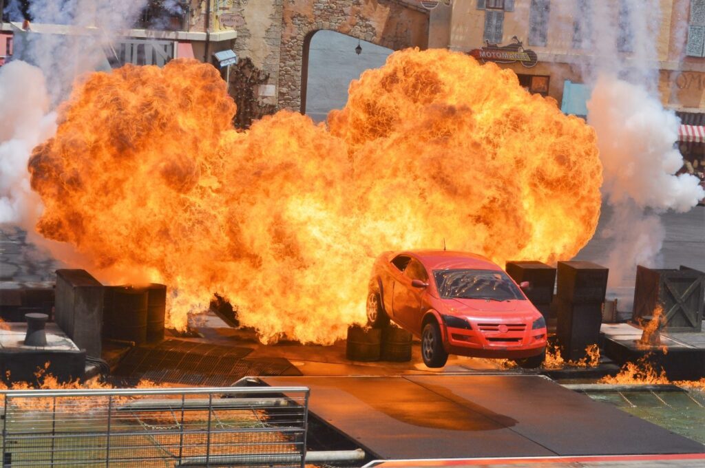 Une voiture rouge saute en l'air avant d'exploser au Moteurs Action Stunt Show, entourée d'accessoires de scène et d'effets de feu spectaculaires avant sa fermeture le 13 mars 2020.