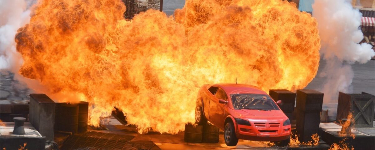 Une voiture rouge saute en l'air avant d'exploser au Moteurs Action Stunt Show, entourée d'accessoires de scène et d'effets de feu spectaculaires avant sa fermeture le 13 mars 2020.