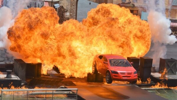 Une voiture rouge saute en l'air avant d'exploser au Moteurs Action Stunt Show, entourée d'accessoires de scène et d'effets de feu spectaculaires avant sa fermeture le 13 mars 2020.