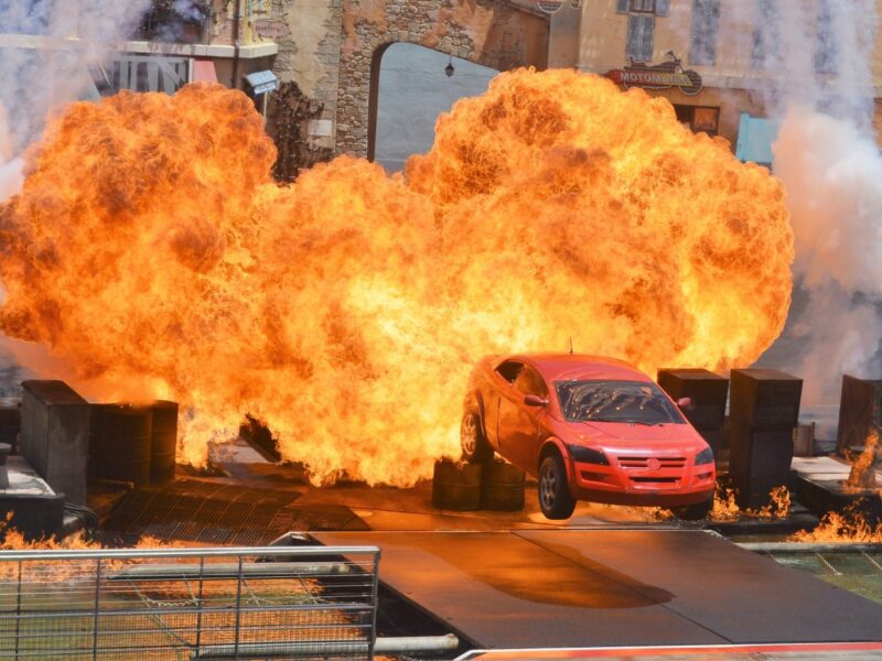 Une voiture rouge saute en l'air avant d'exploser au Moteurs Action Stunt Show, entourée d'accessoires de scène et d'effets de feu spectaculaires avant sa fermeture le 13 mars 2020.