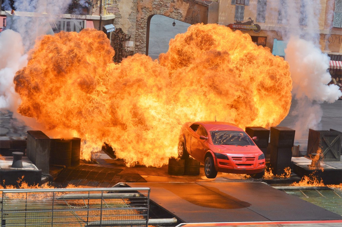 Une voiture rouge saute en l'air avant d'exploser au Moteurs Action Stunt Show, entourée d'accessoires de scène et d'effets de feu spectaculaires avant sa fermeture le 13 mars 2020.