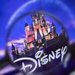 Une loupe se concentre sur le logo Disney avec un château en arrière-plan dans un ciel bleu et violet, soulignant la présence emblématique de Disney et ses obligations en 2020.